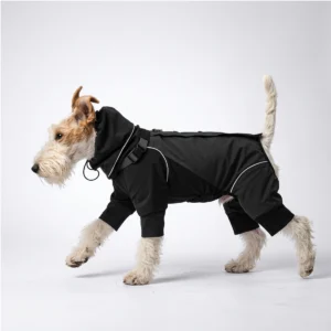 Side profile studio shot of a wire fox terrier walking on plain light gray backdrop, wearing solid black WoofShield four-leg dog rain jacket with integrated attached hood, hood drawstring, reflective piping and elastic fitted leg cuffs